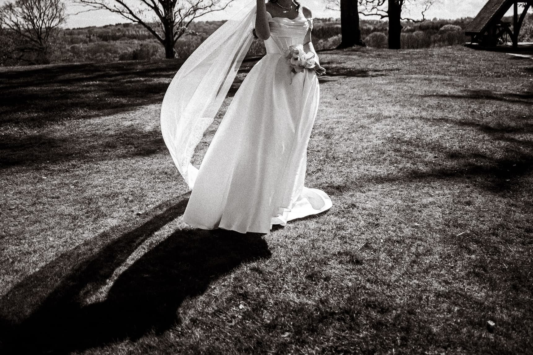 A bride in a flowing gown, her long veil catching the wind, in black-and-white documentary wedding photography by Evocation Photography